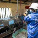 Trabalhador usando uma mesa vibratória para processar minério em uma instalação industrial.