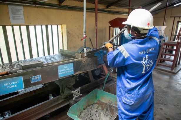 Trabalhador usando uma mesa vibratória para processar minério em uma instalação industrial.