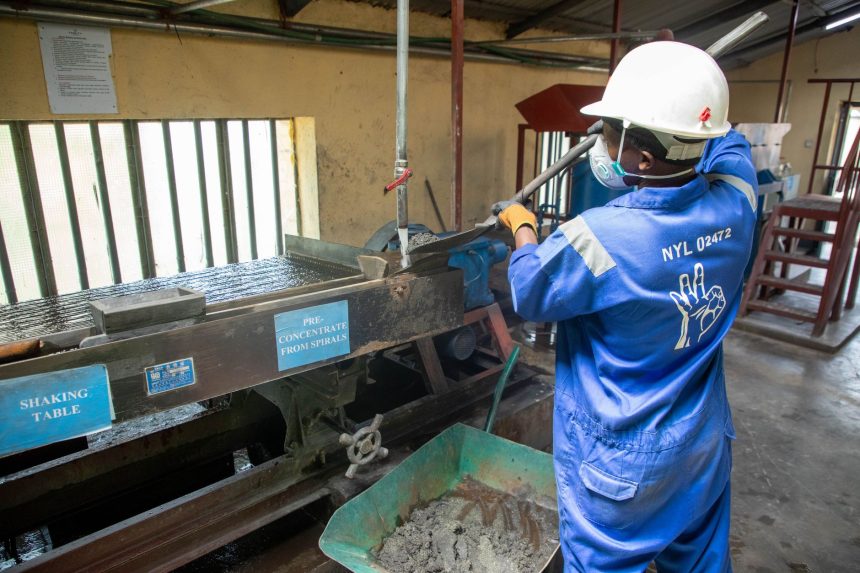 Trabalhador usando uma mesa vibratória para processar minério em uma instalação industrial.