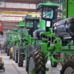 Fileira de máquinas agrícolas verdes dentro de um galpão industrial