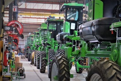 Fileira de máquinas agrícolas verdes dentro de um galpão industrial