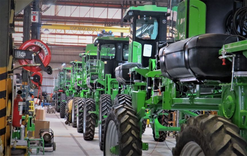 Fileira de máquinas agrícolas verdes dentro de um galpão industrial