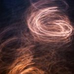Padrões de luz em tons quentes formam uma espiral abstrata sobre fundo escuro