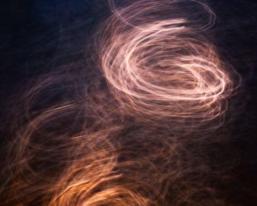 Padrões de luz em tons quentes formam uma espiral abstrata sobre fundo escuro